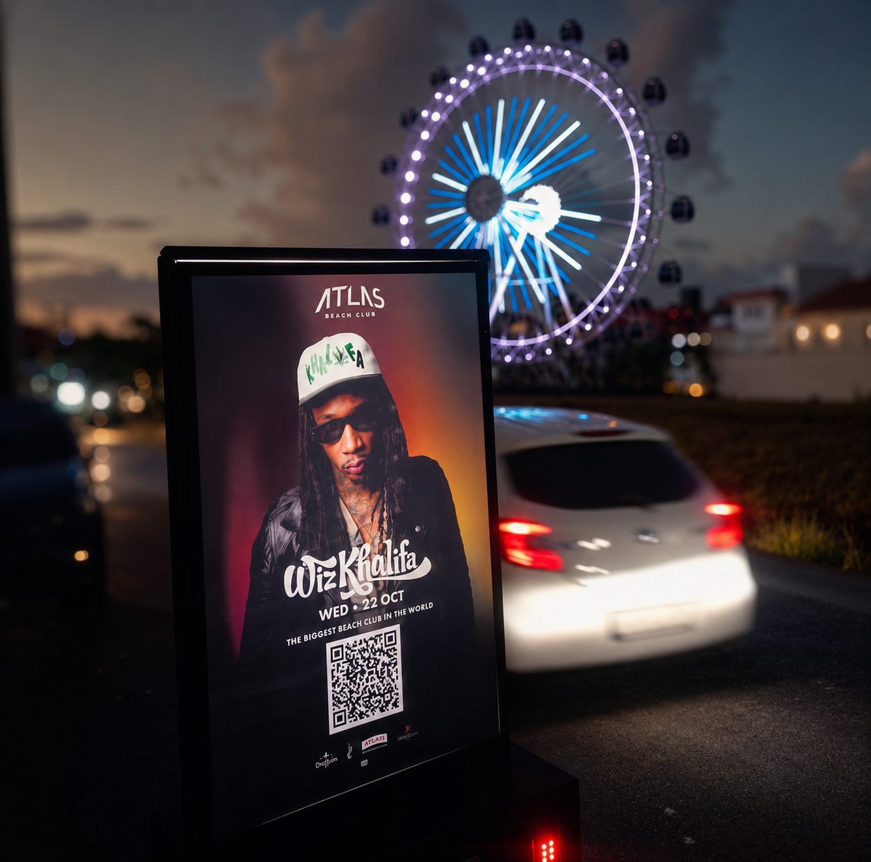 An Imagi Media mobile billboard at dusk advertising an Atlas Beach Club event, with a lit Ferris wheel behind it.